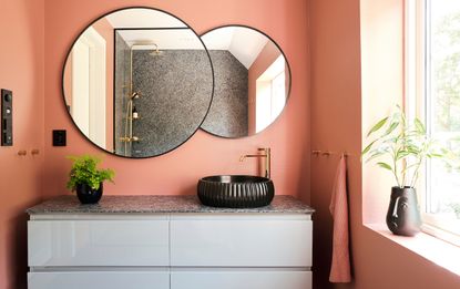 A coral pink bathroom with a double vanity and two circular mirrors