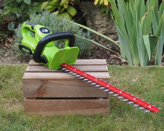 Greenworks cordless hedge trimmer on a box in a garden