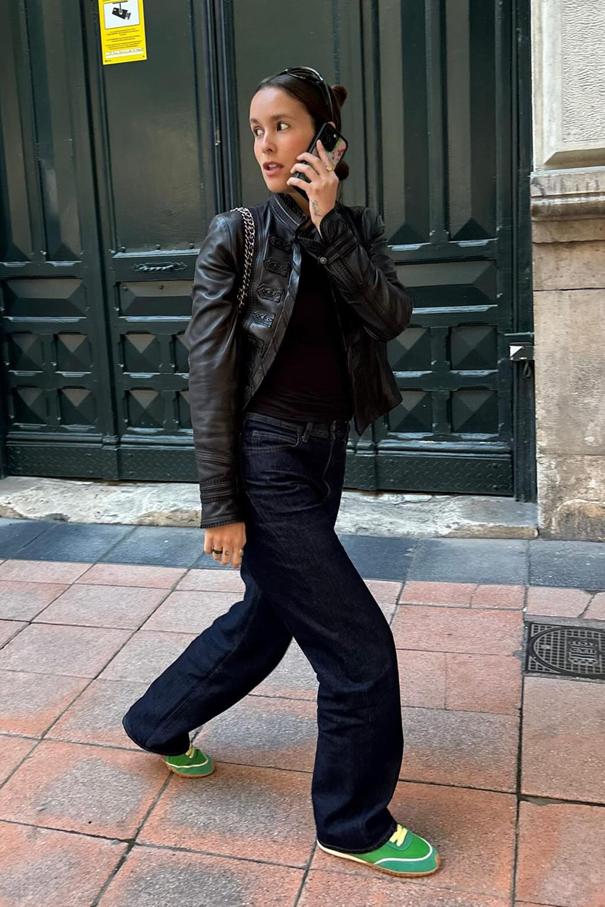 A woman wearing a black leather jacket, jeans, and green sneakers.