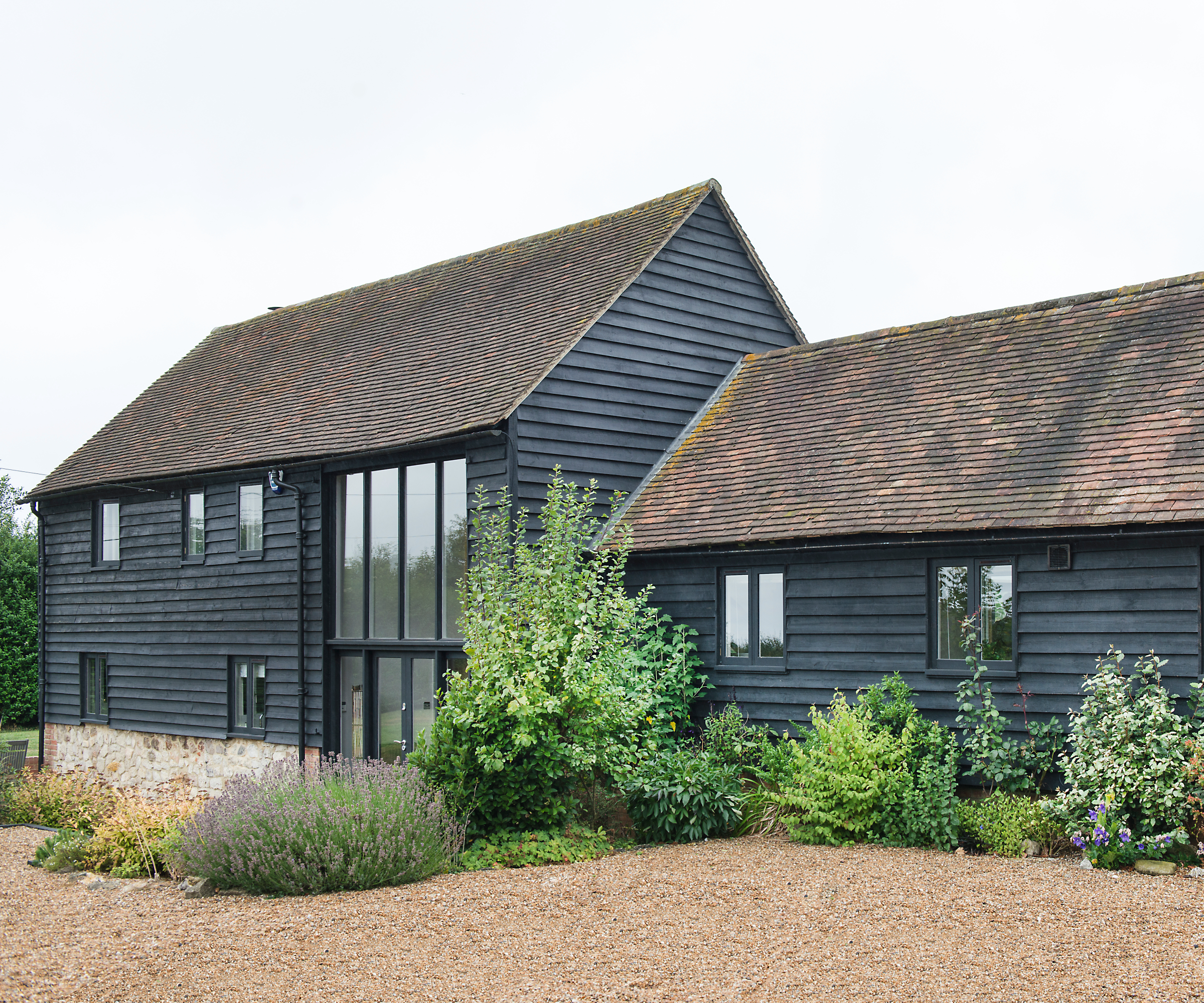 black wooden clad barn with tiled roof, gravel driveway and borders surrounding edges of house