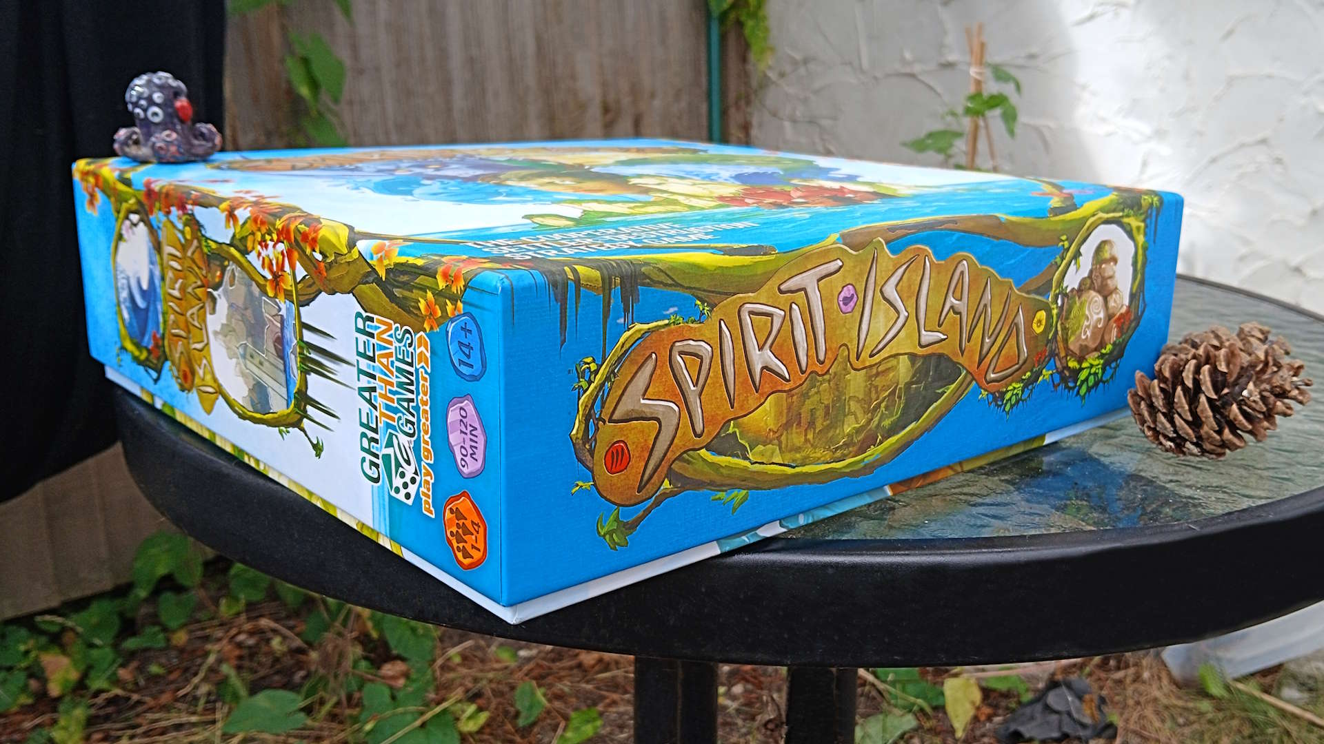 Spirit Island box on its side on a table, with a pinecone to one side