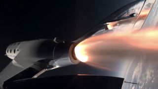 a sleek, silver plane can be seen with a plume of fire shooting out of its exhaust as it soars with earth below it and the blackness of space above it