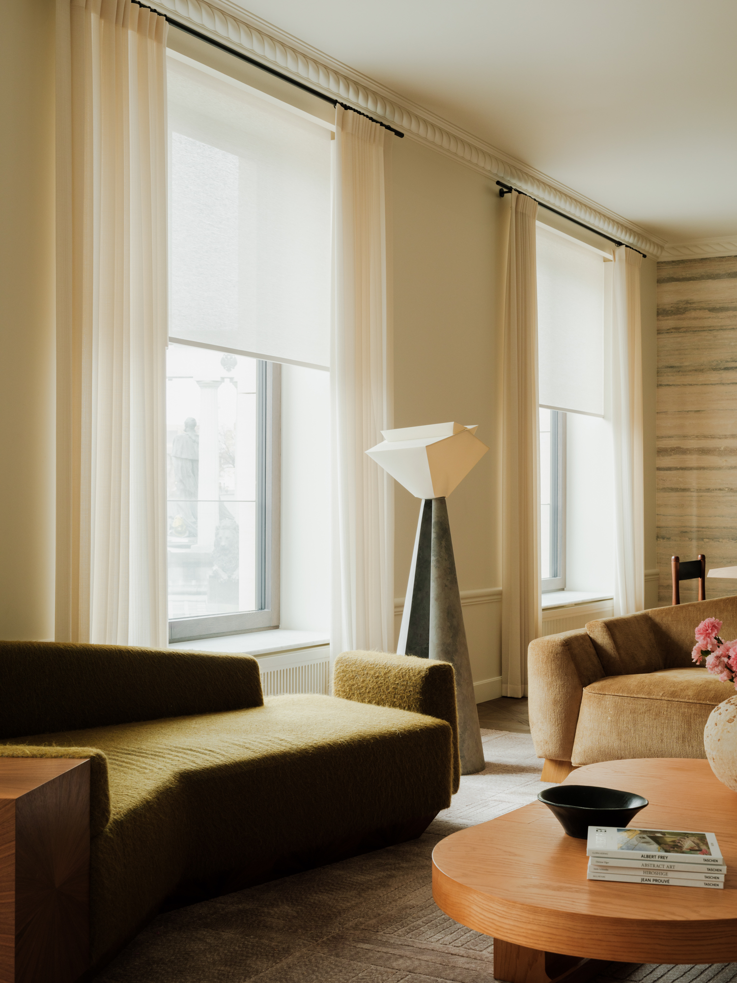 a modern living room that combines minimalism with a warm, mid-century style. There is a geometric olive green sofa and a camel cofa with a wooden coffee table between them and an abstract metal and white floor lamp.