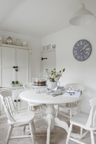 A white kitchen with white painted round table and chairs in breakfast room in an 18th century renovated farmhouse home