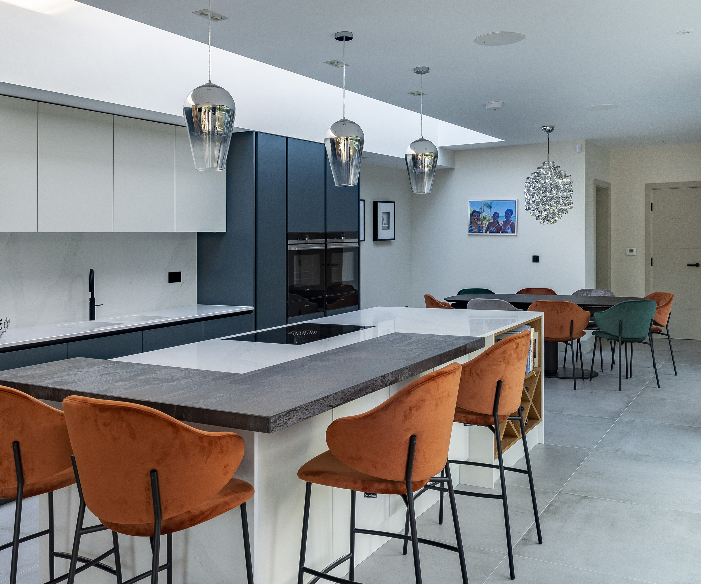 Kitchen island in a modern kitchen extension with white and peacock blue cabinets and orange bar stools