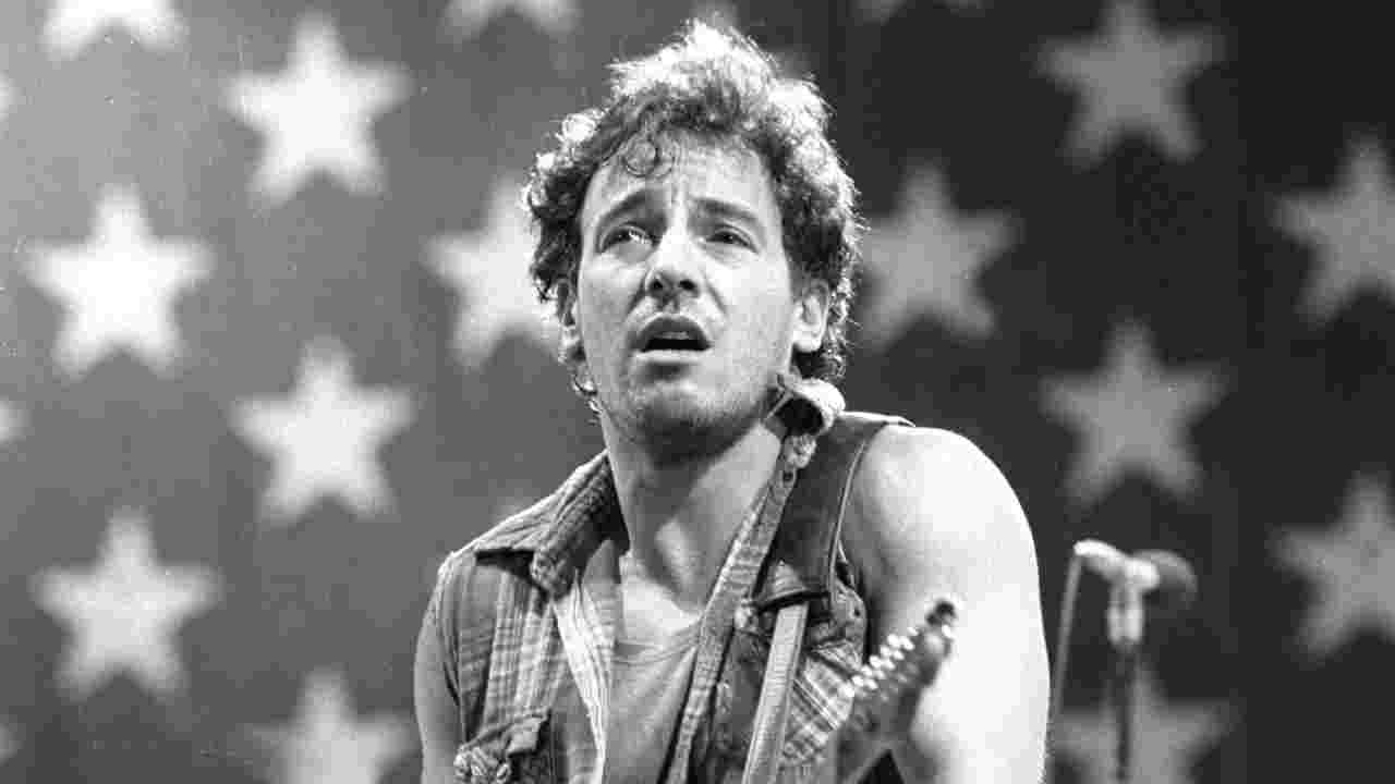 Bruce Springsteen performing onstage in front of a Stars and Stripes flag in 1984
