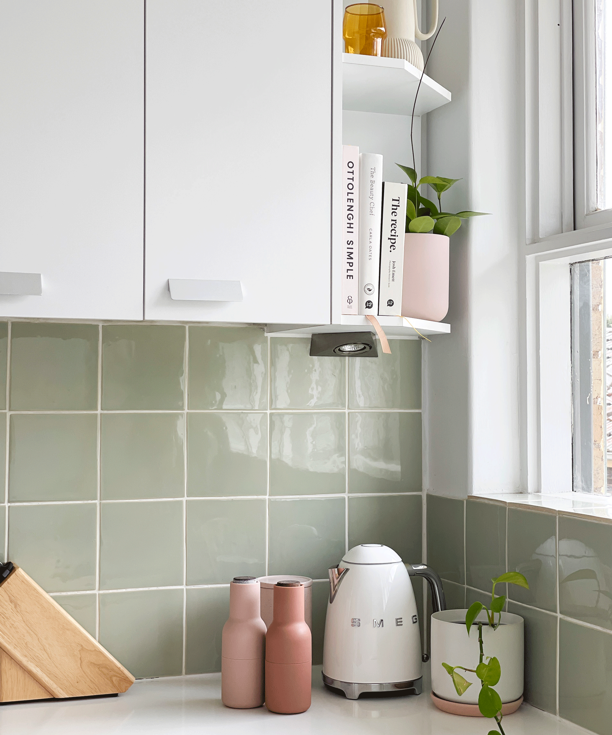 kitchen corner with grey tiles and white cabinetry, a smeg kettle and pink peppermills and salt