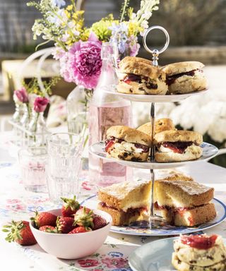 A tiered cake stand containing scones with cream and jam on an outdoor table