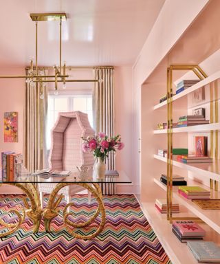 home office with pink color-drenched walls, patterned carpet and gold accents