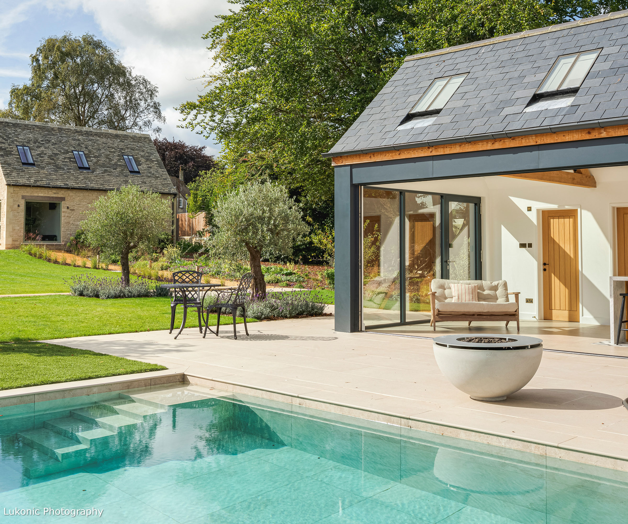 Converted barn with conservation-style rooflights and modern sliding doors leading out to a patio and pool