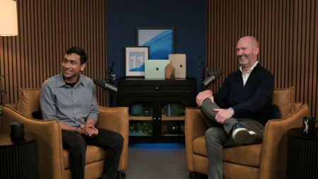 Pavan Davuluri and Brett Ostrum sitting in two arm chairs in front of a display of Surface PCs.