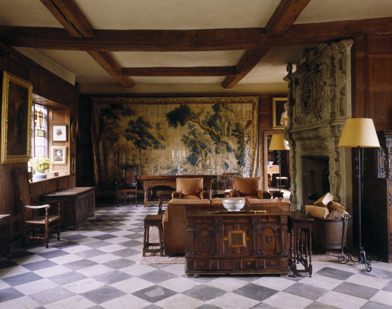 An antiques-filled national trust house houses floral tapestries, ornate woodwork furniture, standing lamps in wrought iron, and chequered tiled floors.