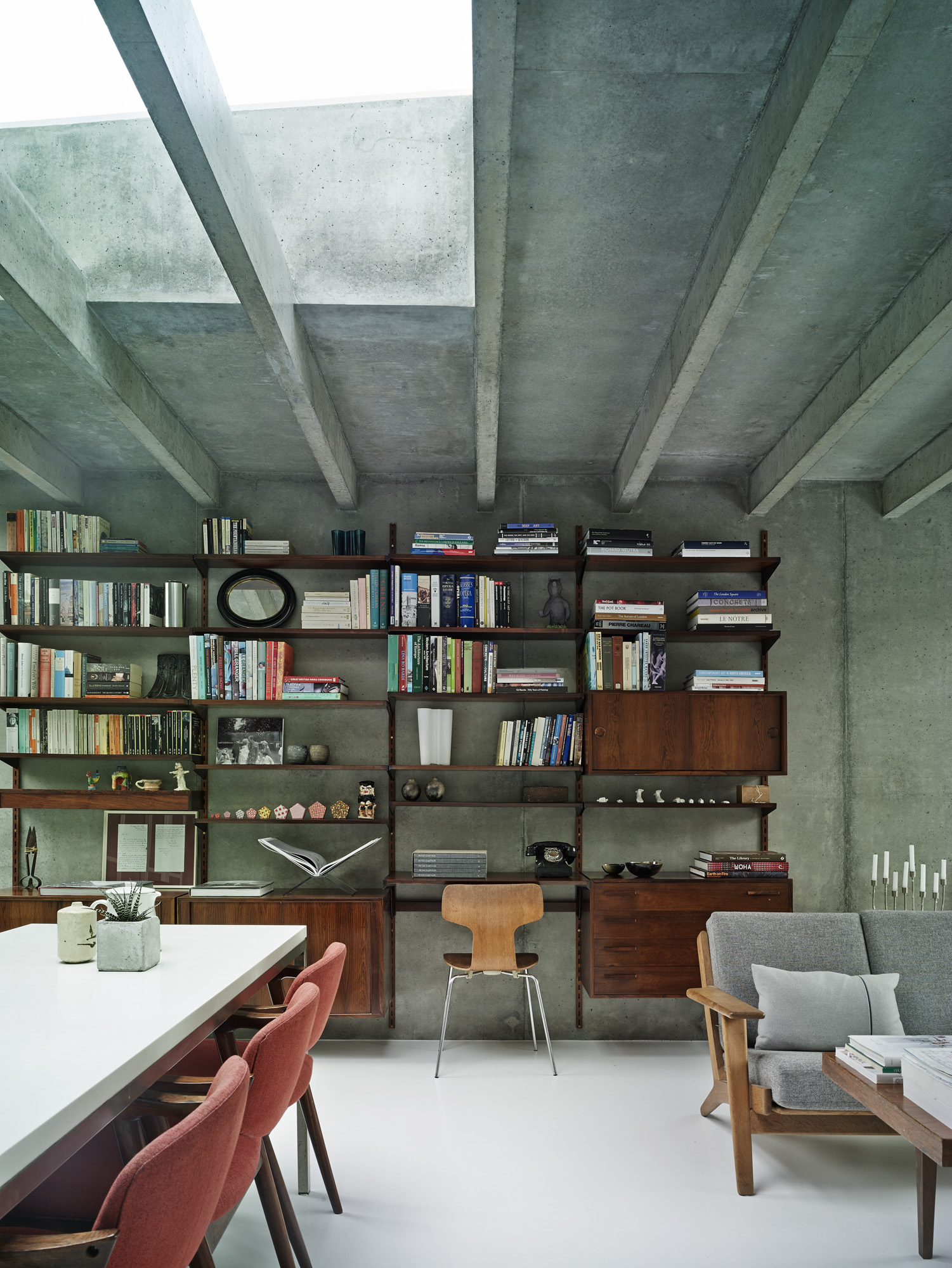 A concrete wall is lined with dark wood bookshelves. Along the ceiling run concrete beams