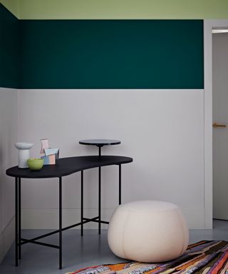 Painted hallway with white and green painted walls. Two different shades of green used, light green and dark green painted strips that cover the top of the wall and ceiling. Unique console table with raised levels in corner, cream pouf and multi-colored rug