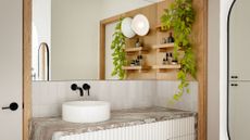 bathroom vanity with full wall length mirror, round sink with black taps, white fluted vanity with grey marble worktop, wood shelves with plants on wall