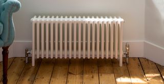 a close up of a cast iron radiator in a white living room with exposed wooden floorboards