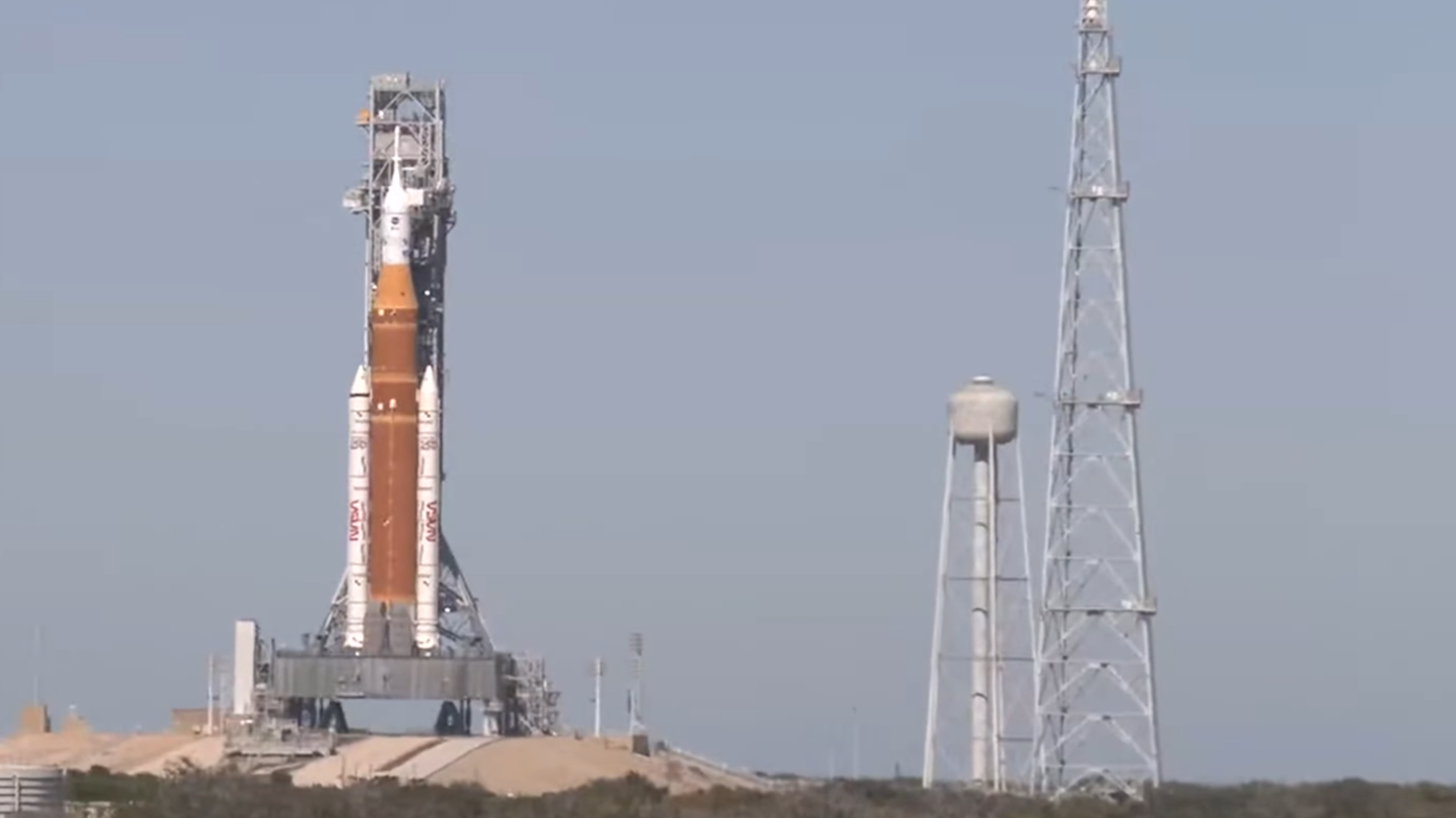 An orange rocket with a white top stands against a dynamic sky.