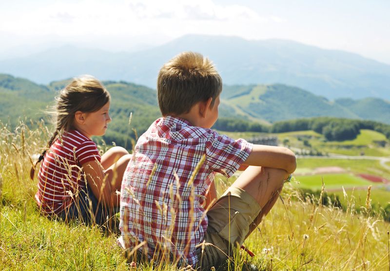 Two children sit on a hillside.