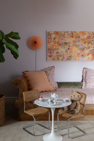 A kids bedroom with a sofa-cum-bed, lavender wall, and a small table for play and work