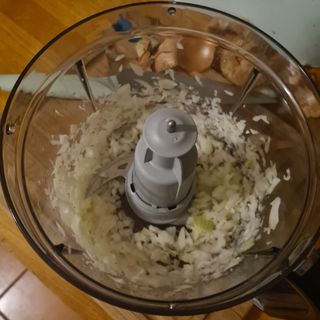 A top down view inside the mixing bowl of the Bosch MultiTalent 8 food processor, showing diced onions and the cutting blade attachment.