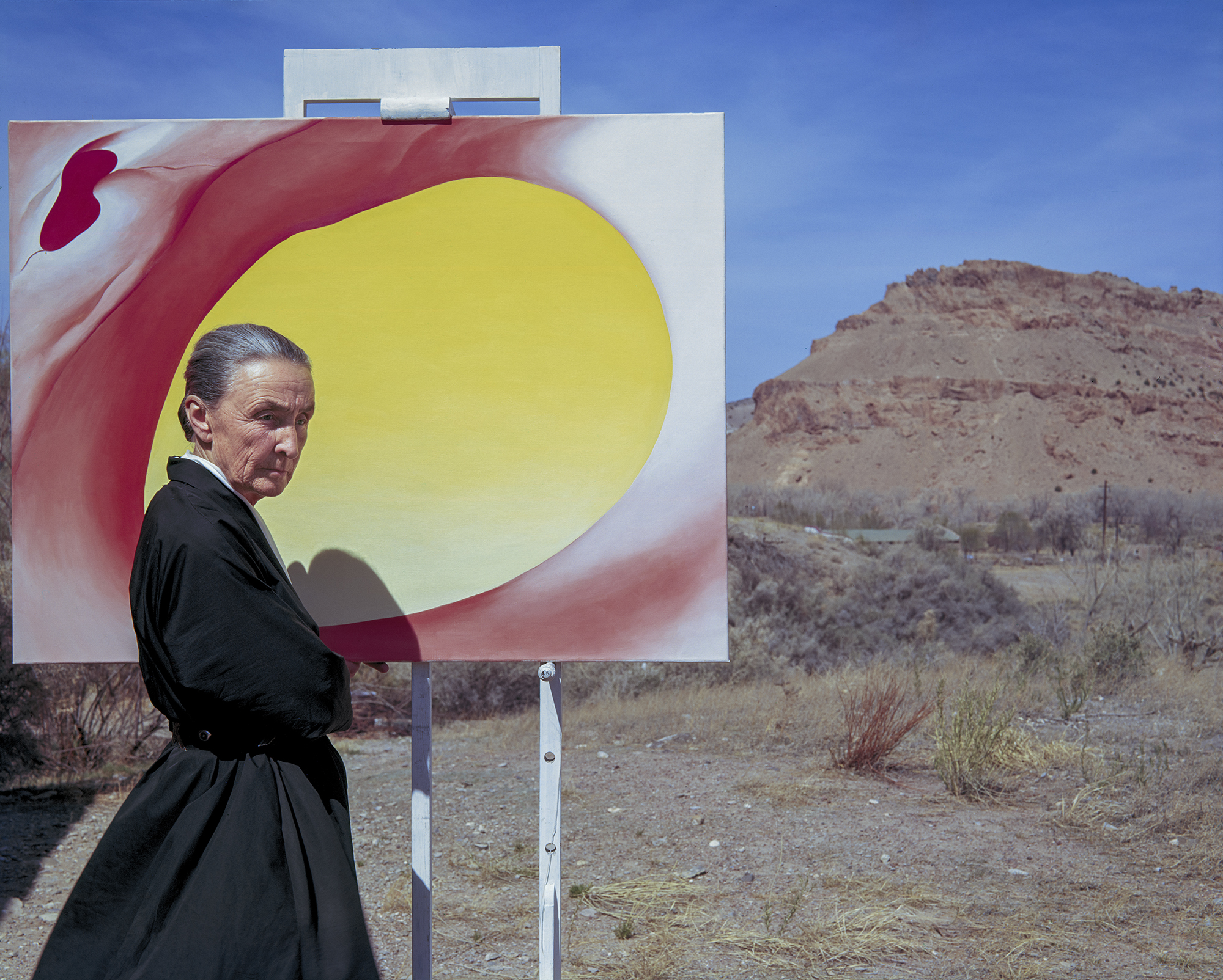 Photo of artist Georgia O'Keeffe stood in front of a bright yellow painting