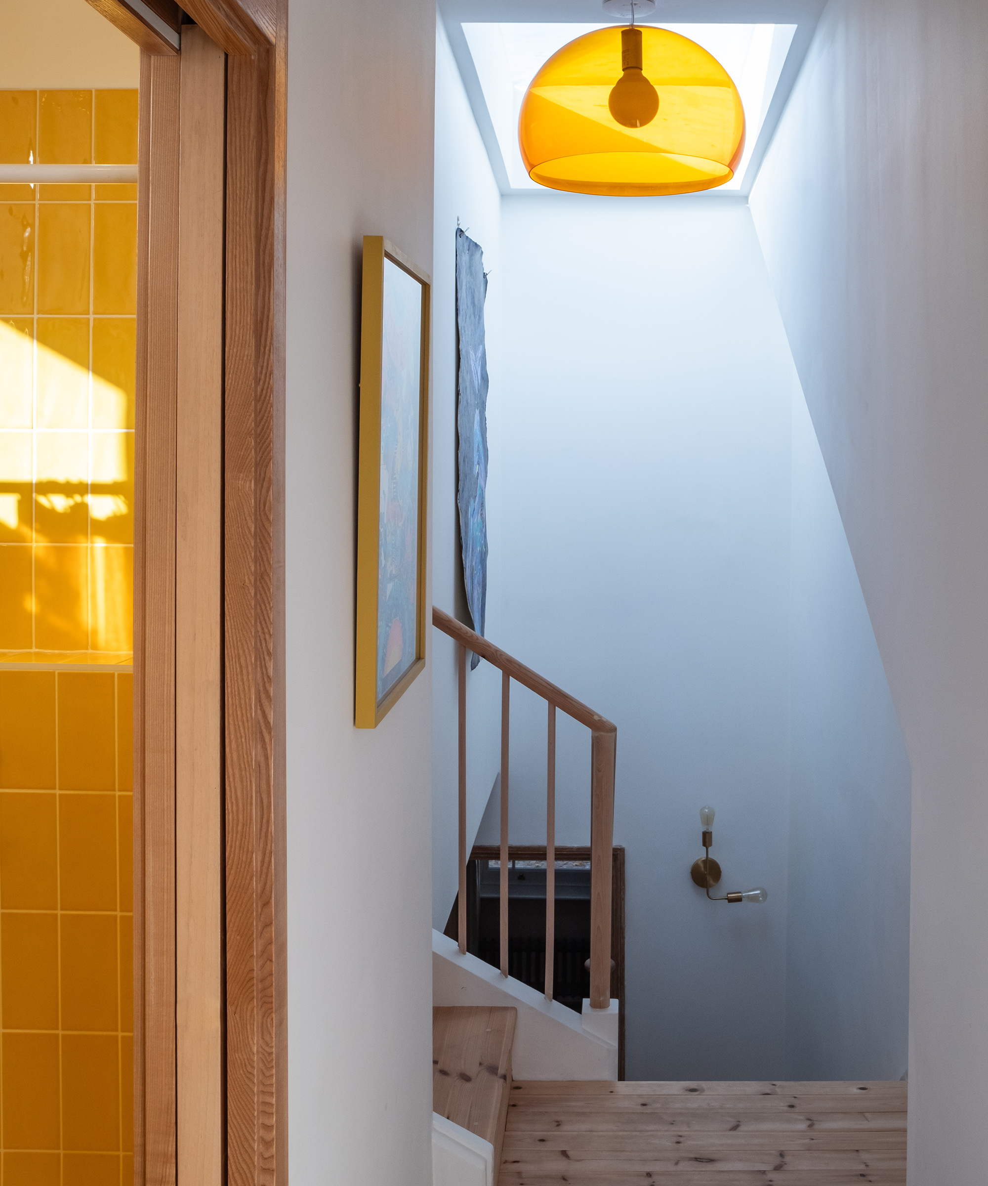 A loft landing with wooden floor and ceiling light. There is a yellow lampshade over the pendant light with yellow bathroom tiles just showing to the left