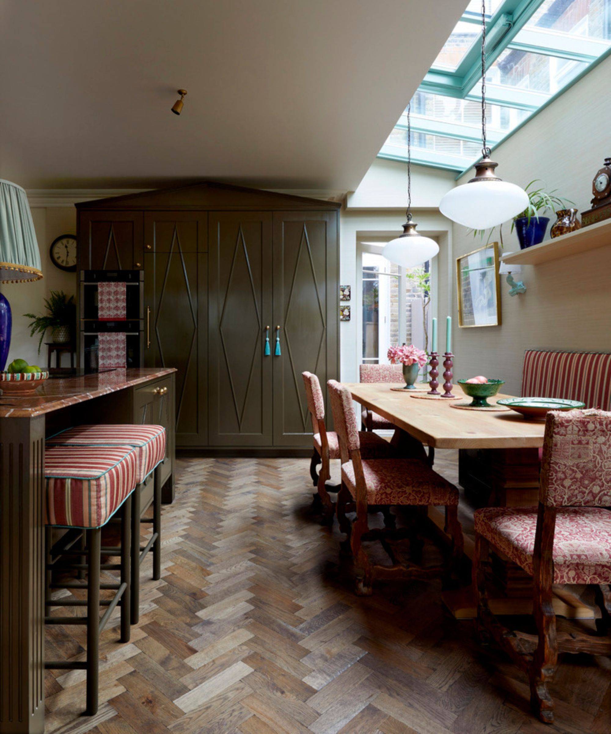 A large kitchen with wooden floors and deep olive green cabinetry layered with deep red accessories