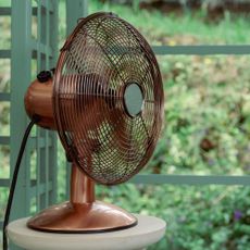 Copper desk fan on a stand in front of green trellis with views to garden greenery