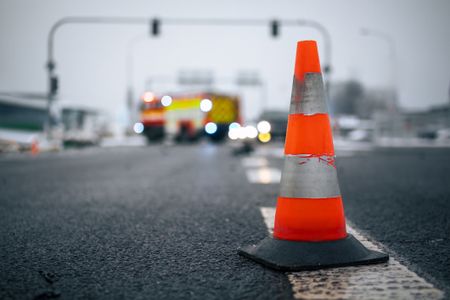 Warning traffic cone on road against fire engine of firefighters at car accident on winter day.