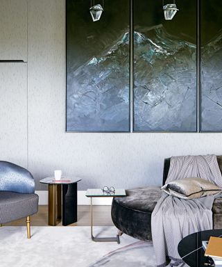 A minimalist living room with white walls and a dark gray velvet chair in front of dark wall art