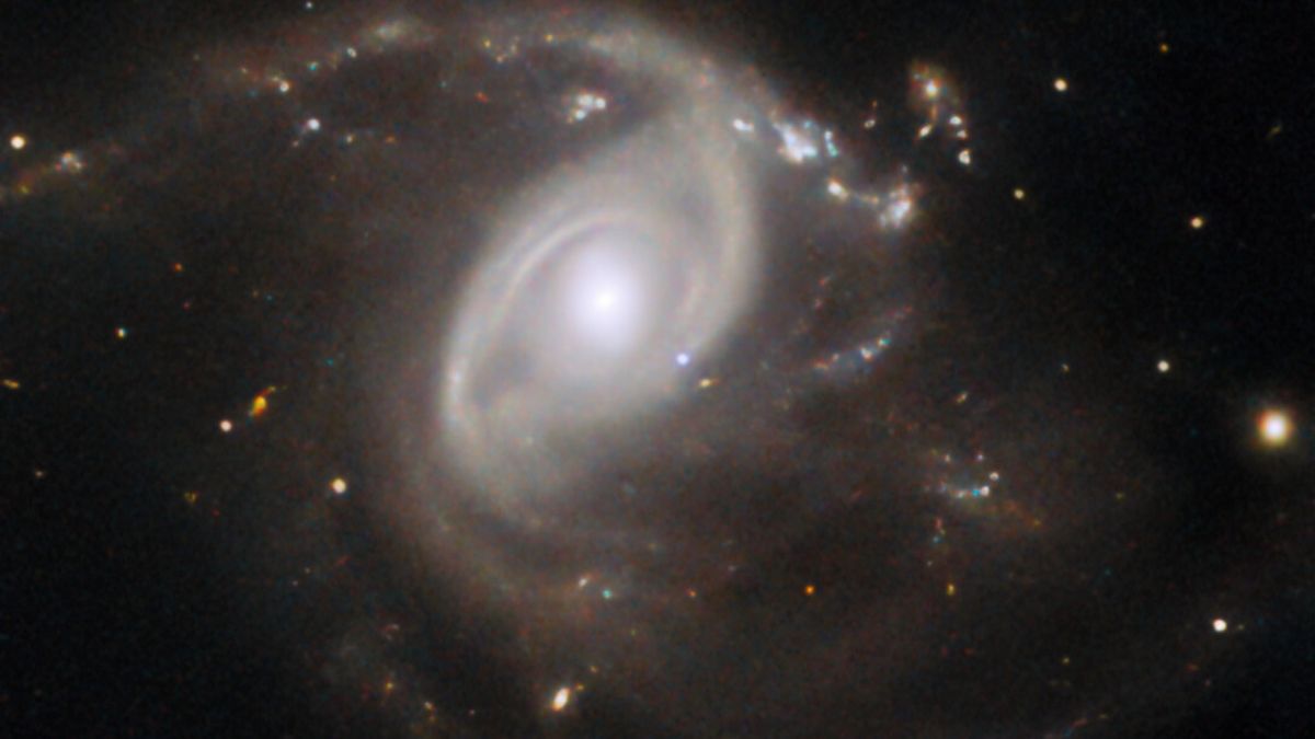 hubble telescope image of a spiral galaxy, with a pale blue dot just below and to the right of the galactic nucleus