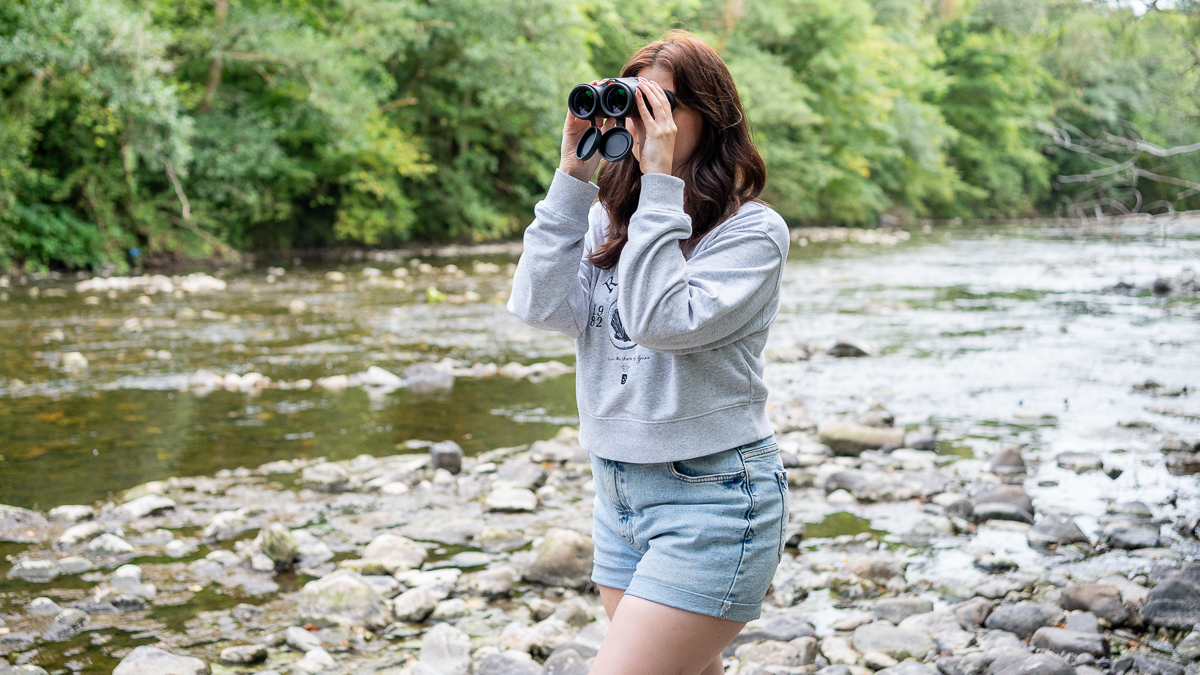 woman using the Celestron Outland X 10x42 binoculars next to a river