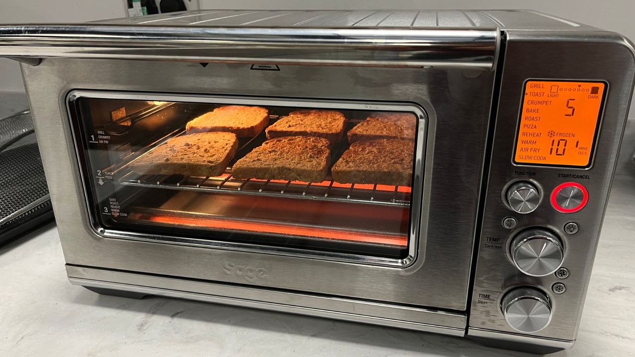 The Breville the Smart Oven Air Fryer Toaster Oven making toast on test. It is lit from below by the heating element and the screen on the left hand side is lit up in orange, with the functions and times listed.