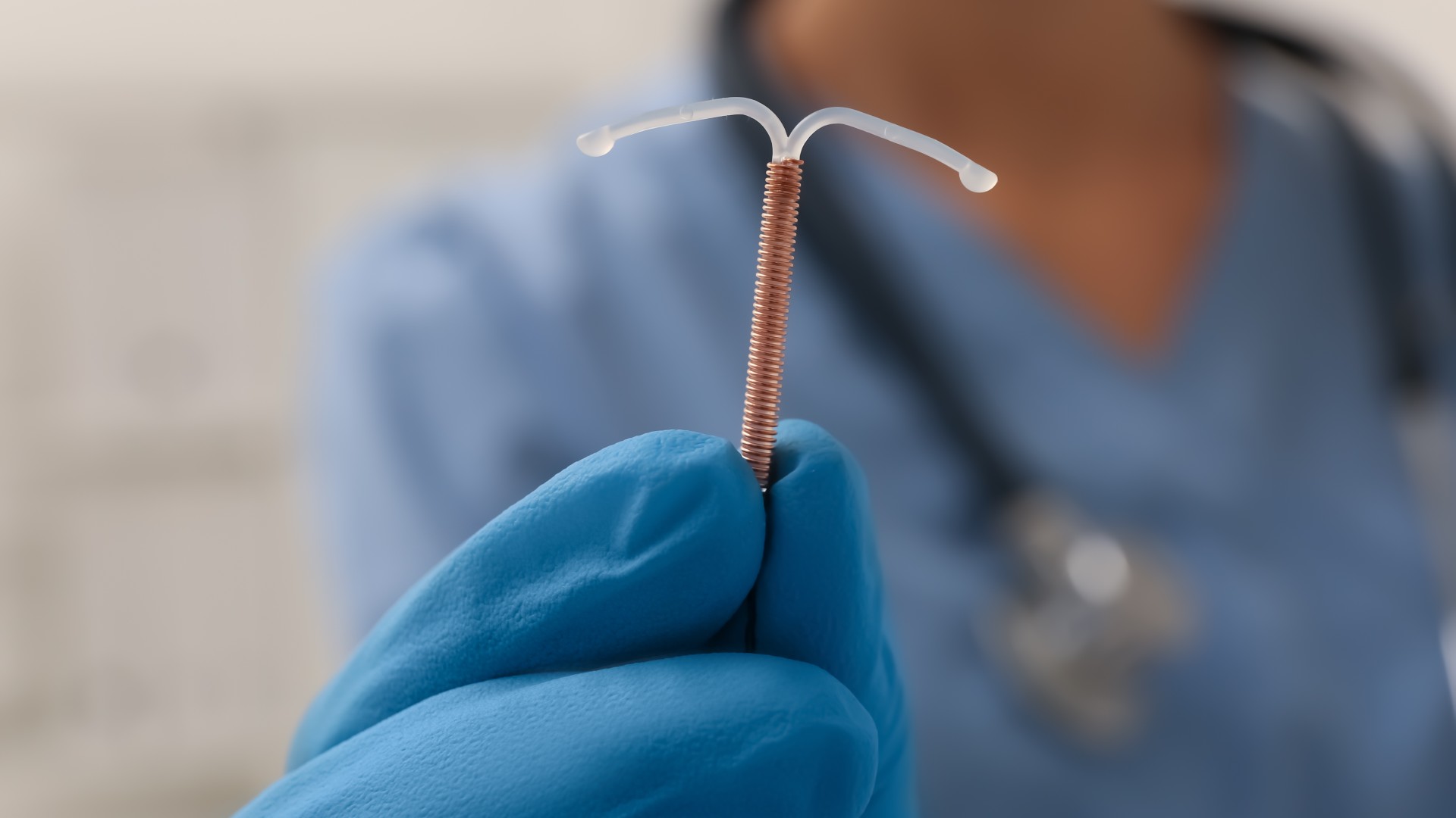 Doctor holding a T-shaped intrauterine device (IUD) made out of copper on blurred background, close up_New Africa via Shutterstock