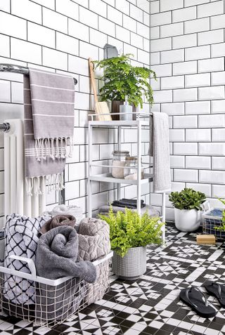 A modern black and white bathroom with white metro wall tiles and ornately patterned monochome bathroom floor with white towel storage unit, and white wire basket
