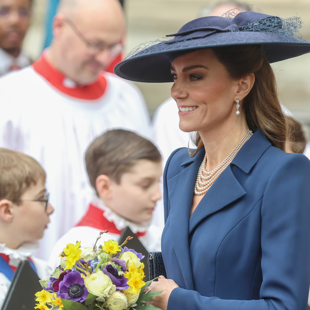 Princess Kate wearing a blue coat and hat holding flowers in front of choir boys