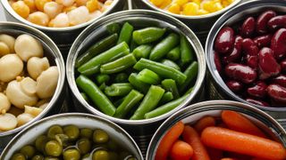 Canned vegetables in opened tin cans on kitchen table.