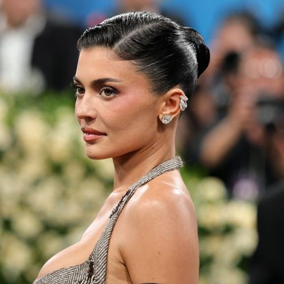 a woman photographed in front of a crowd wearing a tight bun and silver earrings