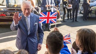 King Charles III waves and greets schoolchildren with Union Jack flags as he arrives to meet with members and staff of the association "Project Zero", an organisation dedicated to engaging young people in positive activities, promoting social inclusion and strengthening community cohesion, during a visit of the center in Walthamstow, in east London, on October 18, 2022.