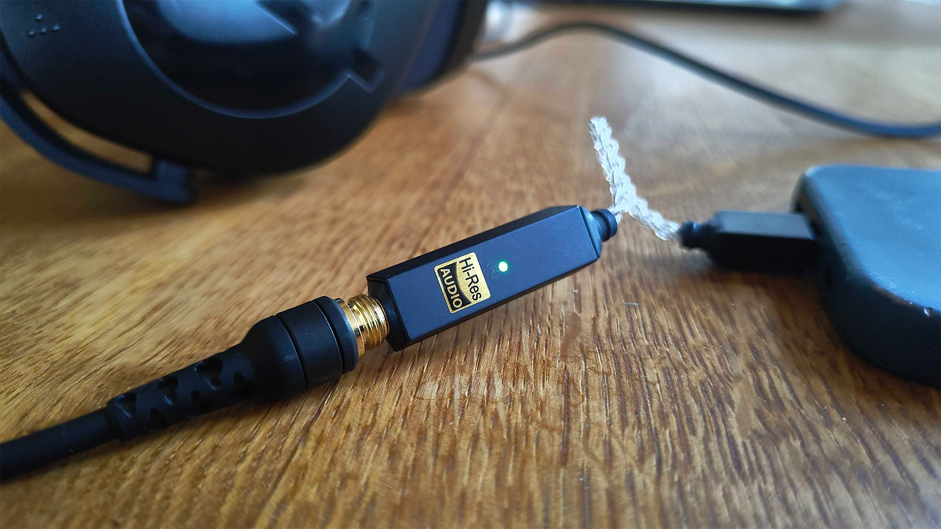 iFi Go Link 2 DAC on wooden table top connected between headphones and smartphone