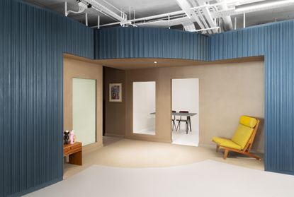 A room with blue walls, a yellow chair and a separate open room with a table and two chairs. 