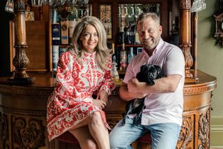 The couple sitting at the bar in the house with their pug dog in the man's arms