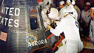 technicians in white clean room suits help an astronaut in a silver spacesuit and white helmet climb into a spacecraft for launch