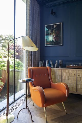 living room with an orange accent chair and blue wall by Kitesgrove