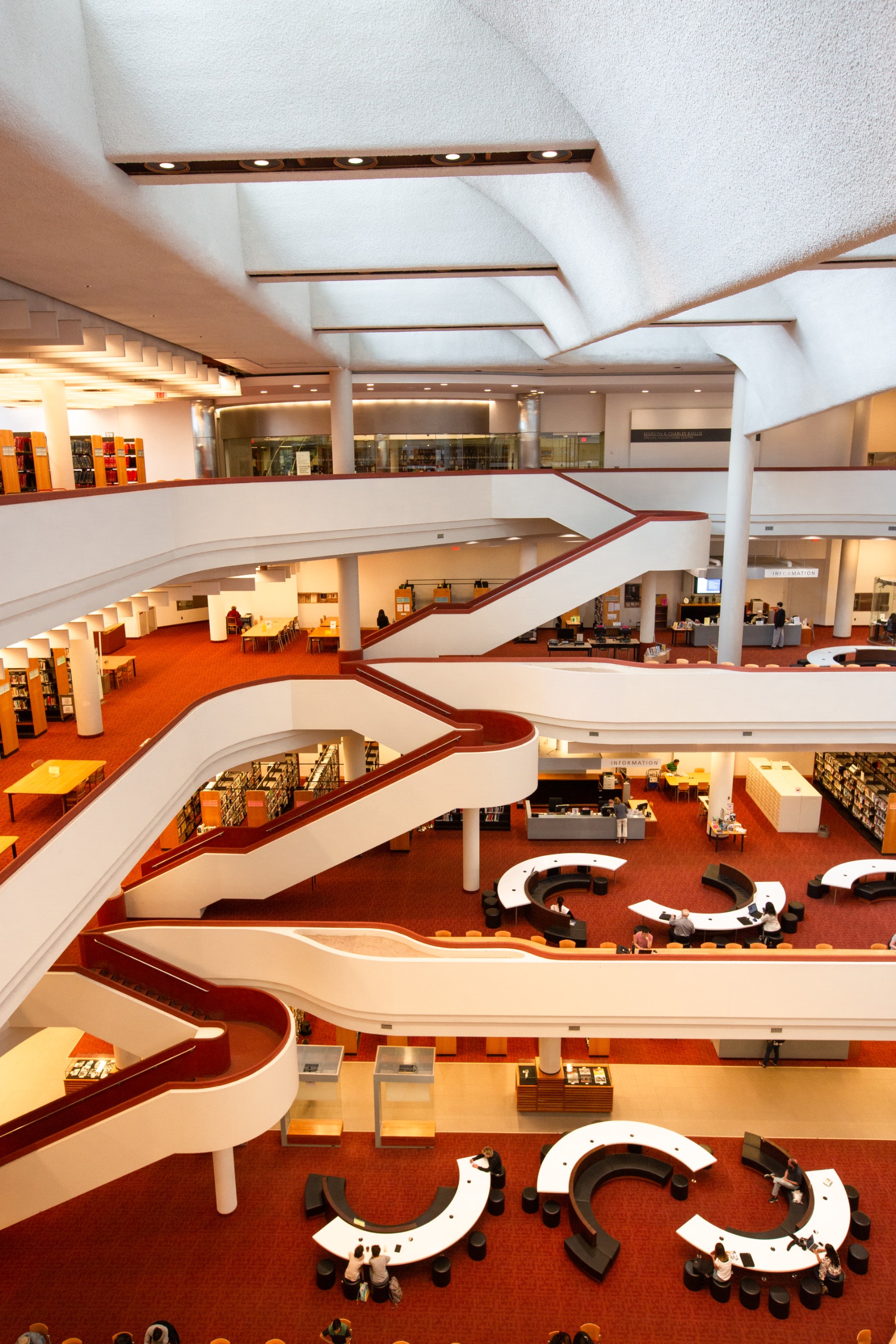Aerial view of an architecturally striking library with curvaceous staircases, a red-tinted floor, and white structure, along with semi-circular desks.