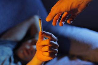 A man hands a marijuana cigarette to someone