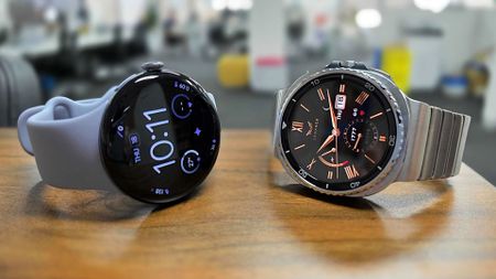 Google Pixel Watch 4 and Samsung Galaxy Watch 8 Classic placed side by side on bench top