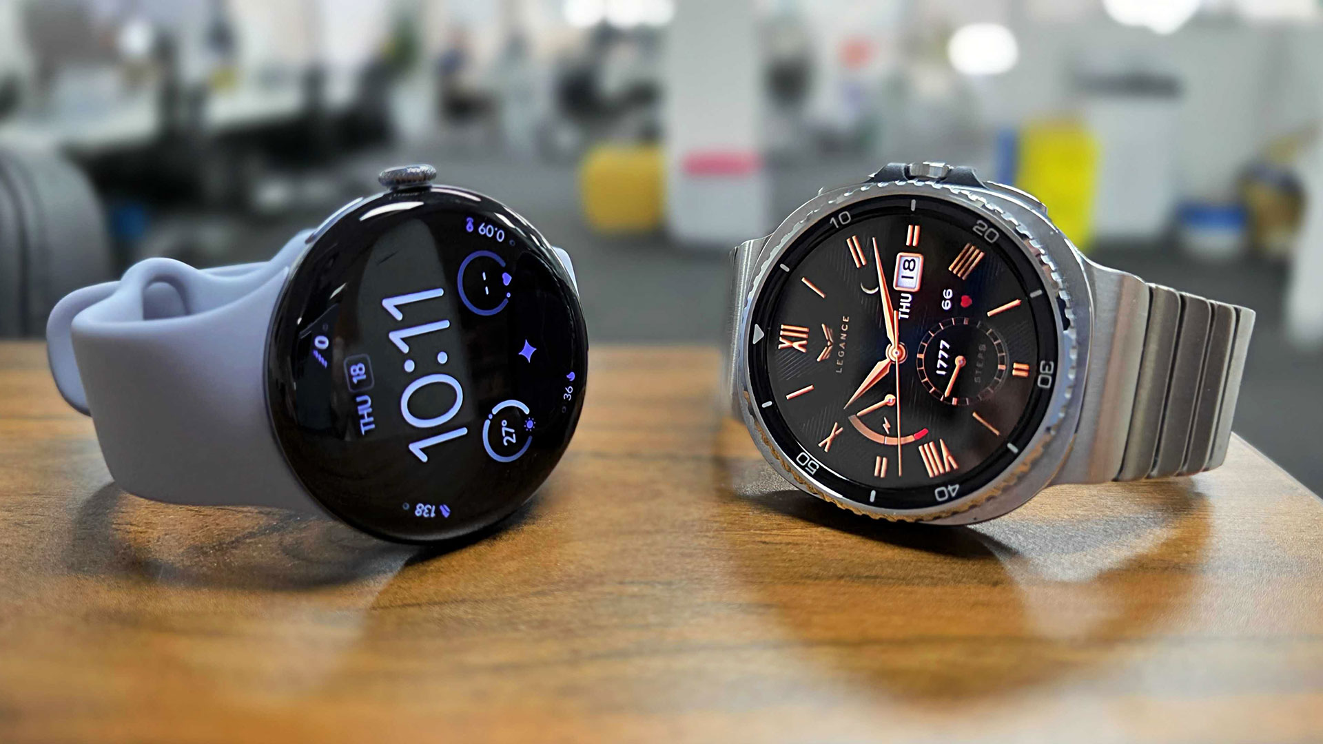 Google Pixel Watch 4 and Samsung Galaxy Watch 8 Classic placed side by side on bench top