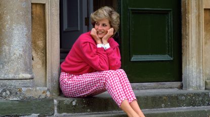 Princess Diana in a pink cardigan and gingham trousers sitting on the steps of Highgrove House
