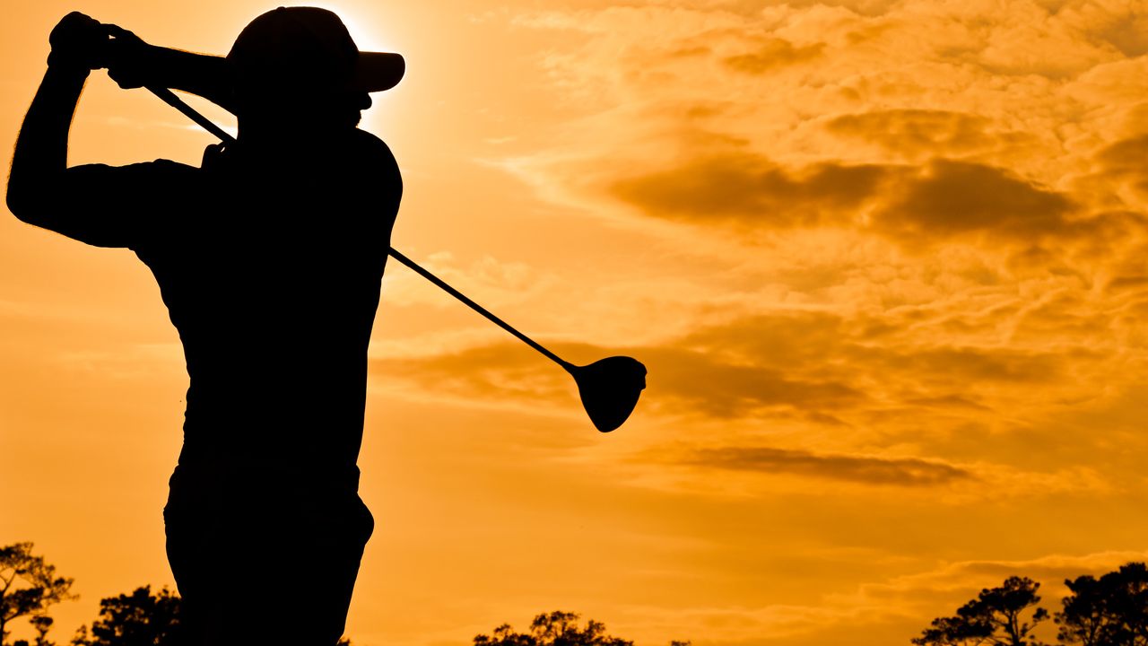 Silhouette of a golfer after hitting a tee shot with driver, set against an orange sunset background